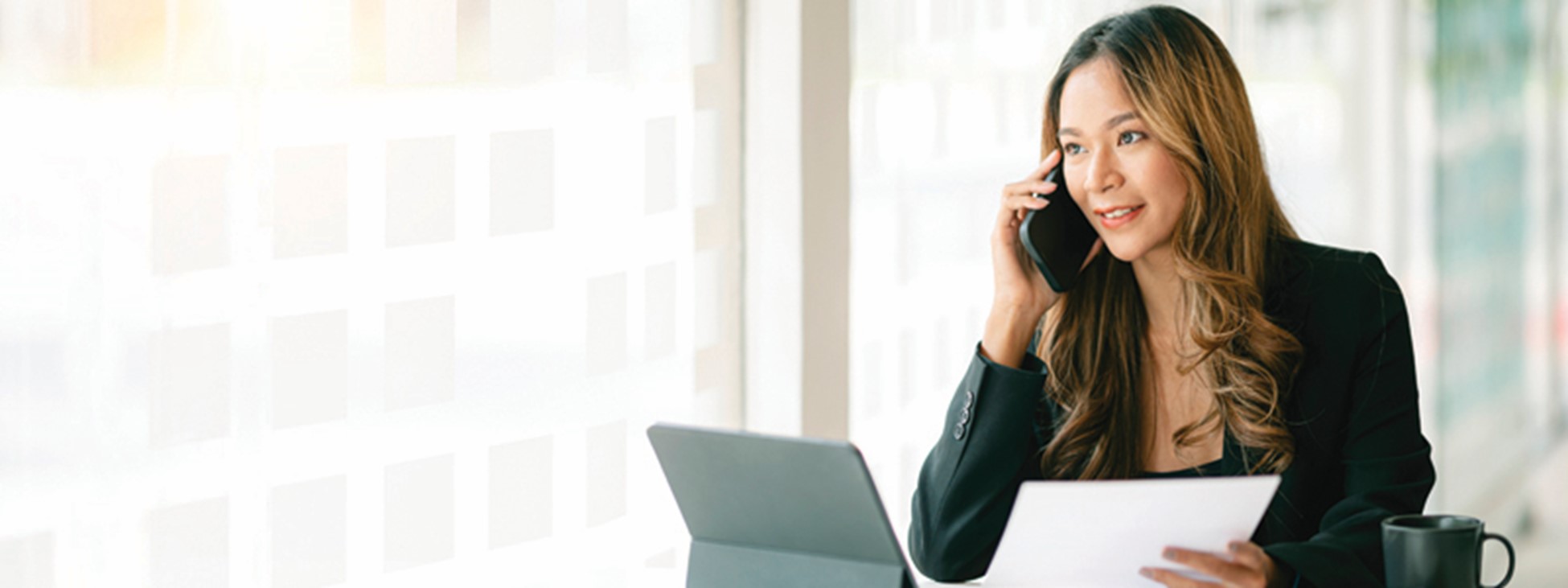 young woman talking on the phone in front of a computer holding a piece of paper.