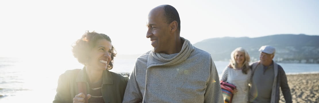 Two mature, smiling couples walking on a beach